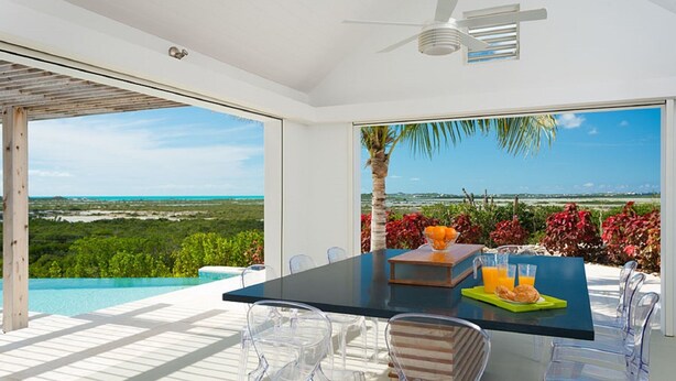Un área de comedor exterior moderna con vista despejada al océano y vegetación.