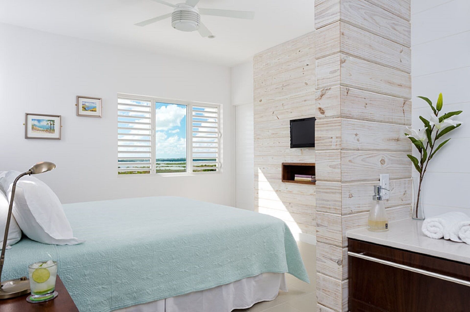 Un dormitorio con cama, escritorio, silla, lámpara, televisor y ventana con persianas.