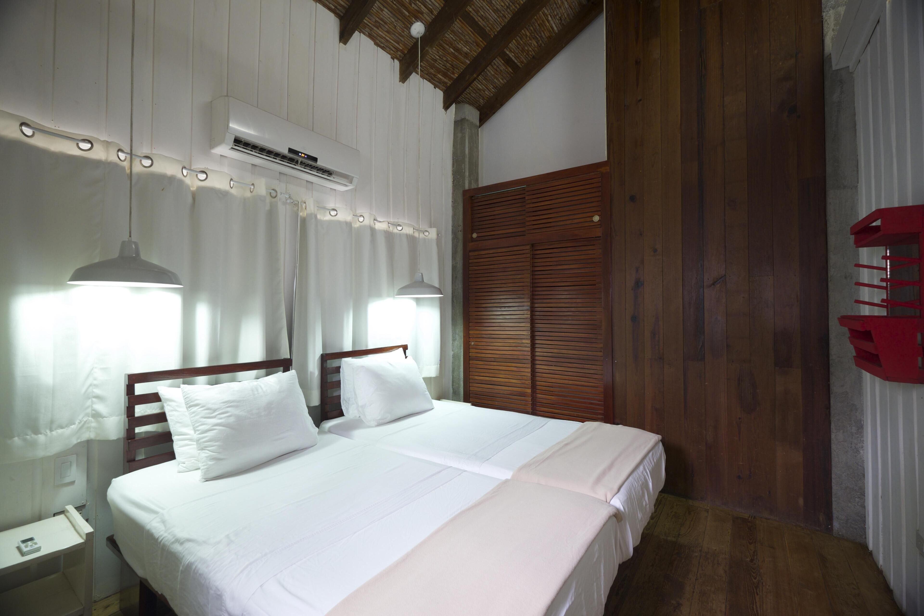 Un dormitorio con cama de madera, cortinas blancas y un equipo de aire acondicionado.