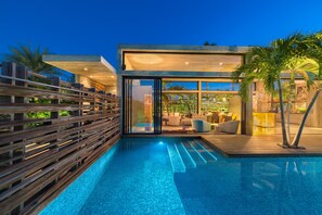 A modern poolside area with a wooden deck, a glass-enclosed lounge, and a clear view of the pool. - Villa Islander in Grace Bay (Grace Bay)