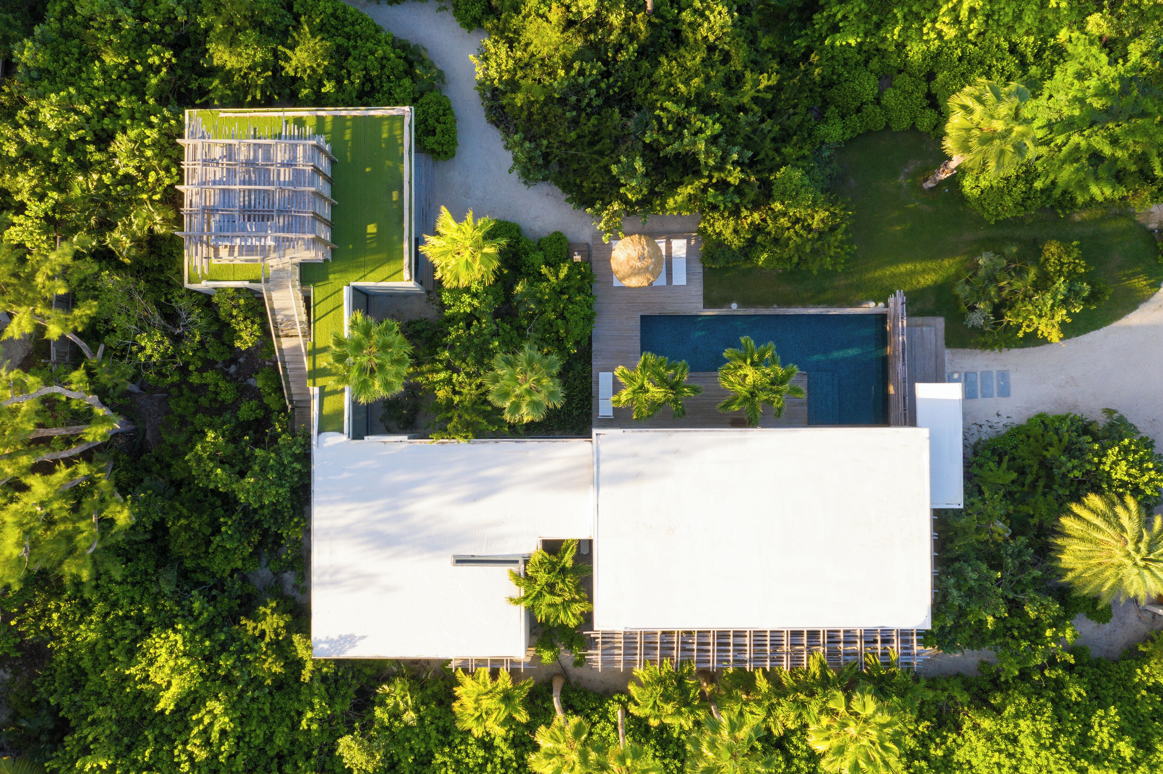 Vista aérea de um resort moderno com piscina, área de deck coberta e vegetação exuberante ao redor da propriedade.