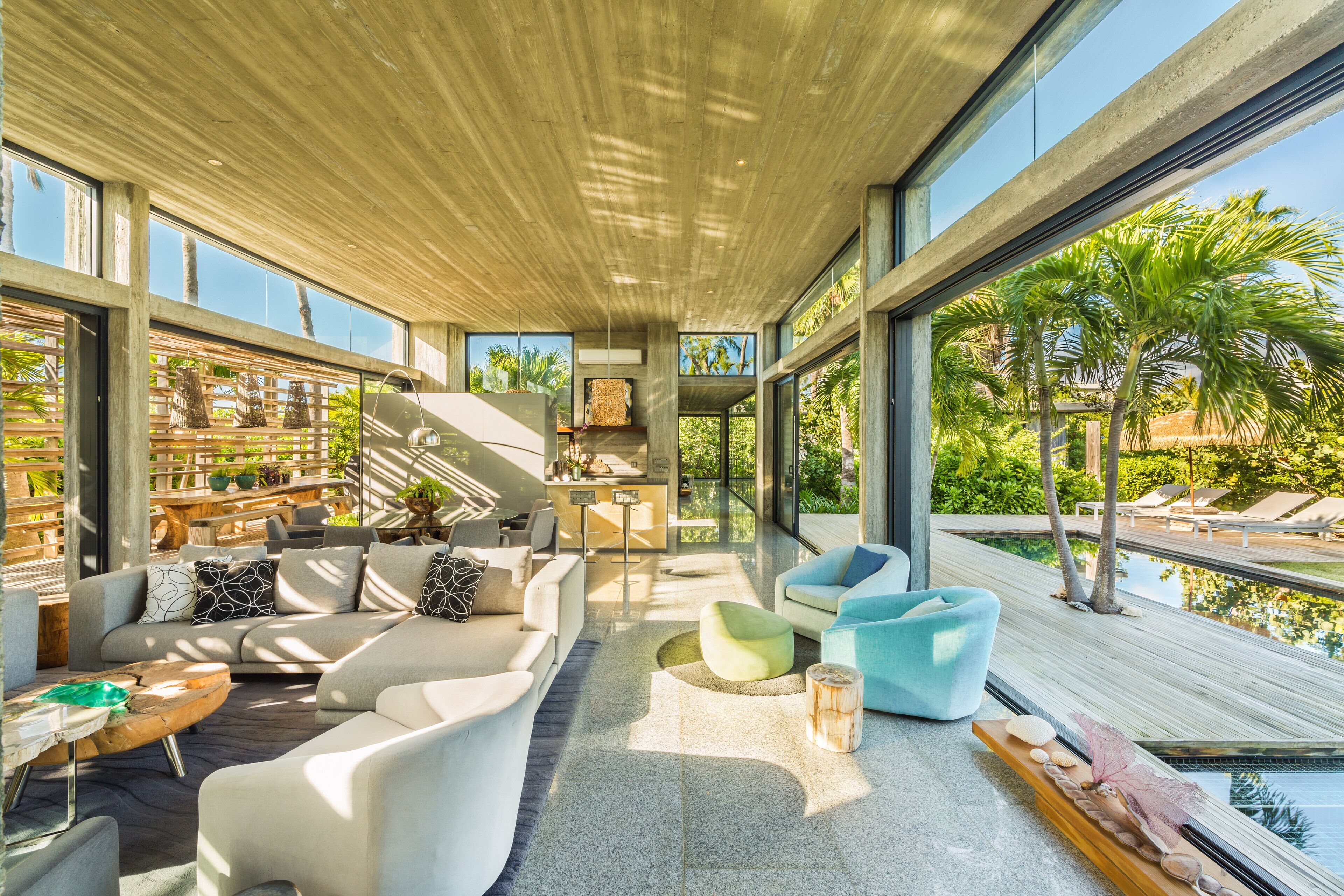 A modern living room with a large window, a sofa, a coffee table, and a poolside view.