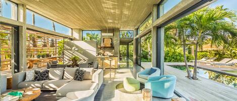 A modern living room with a large window, a sofa, a coffee table, and a poolside view.