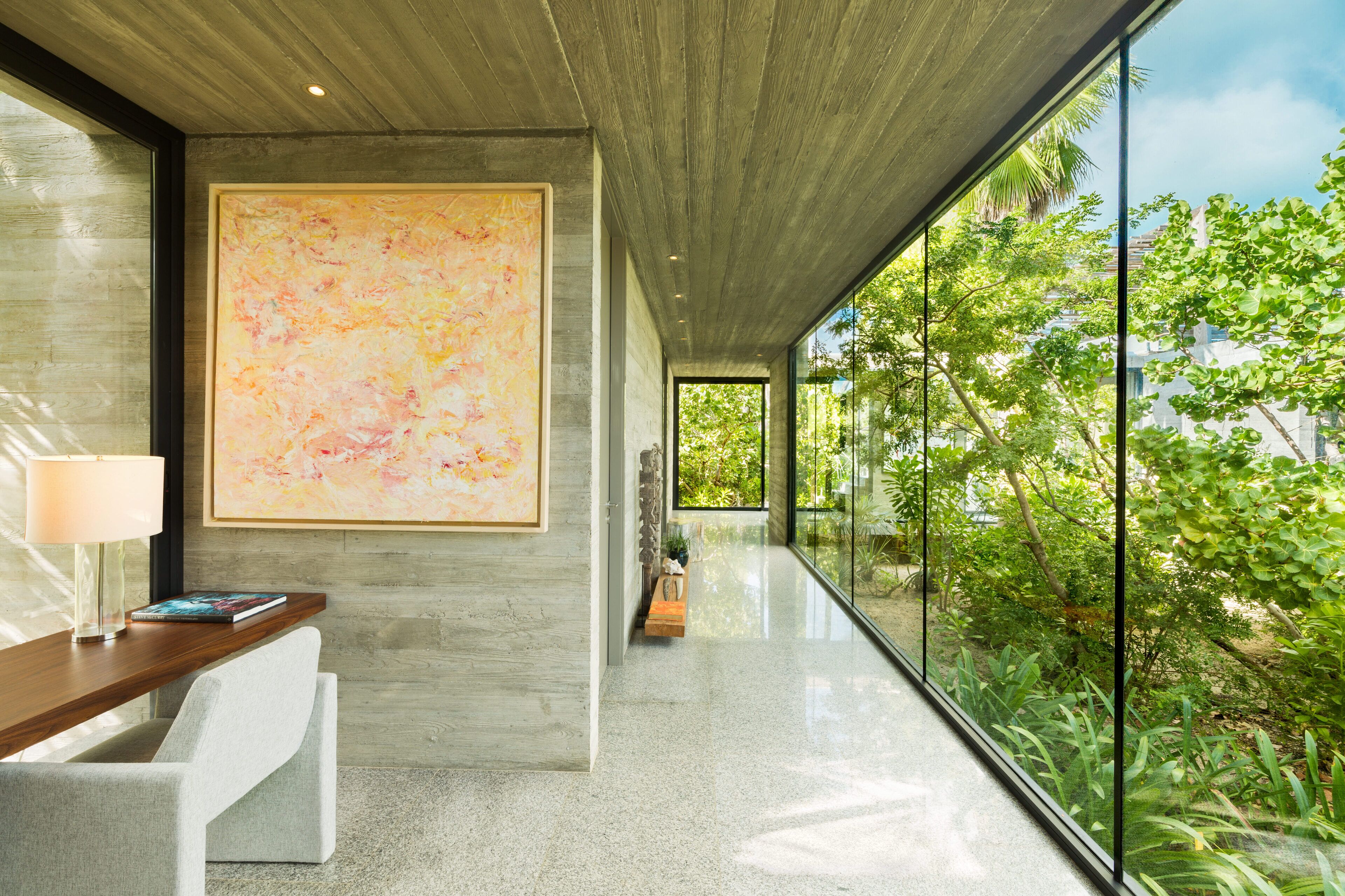A modern interior with a large abstract painting, a wooden desk, and a view of greenery through large windows.