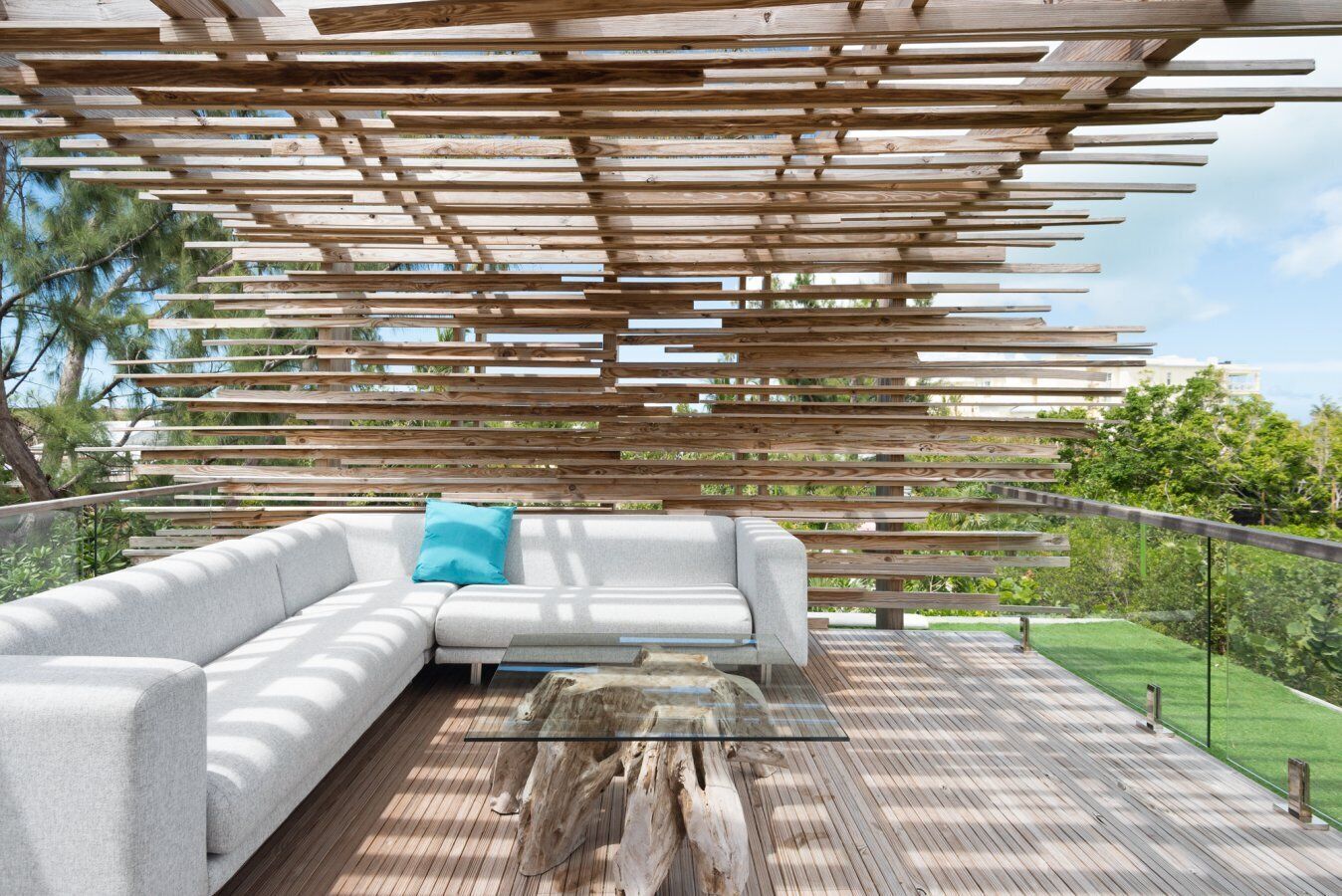 A modern outdoor seating area with a wooden pergola, a white sofa, and a glass coffee table on a wooden deck.