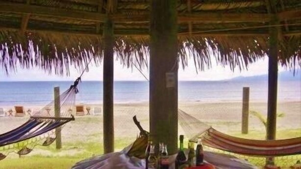 Escena costera con una mesa para dos, una hamaca y vista al mar.