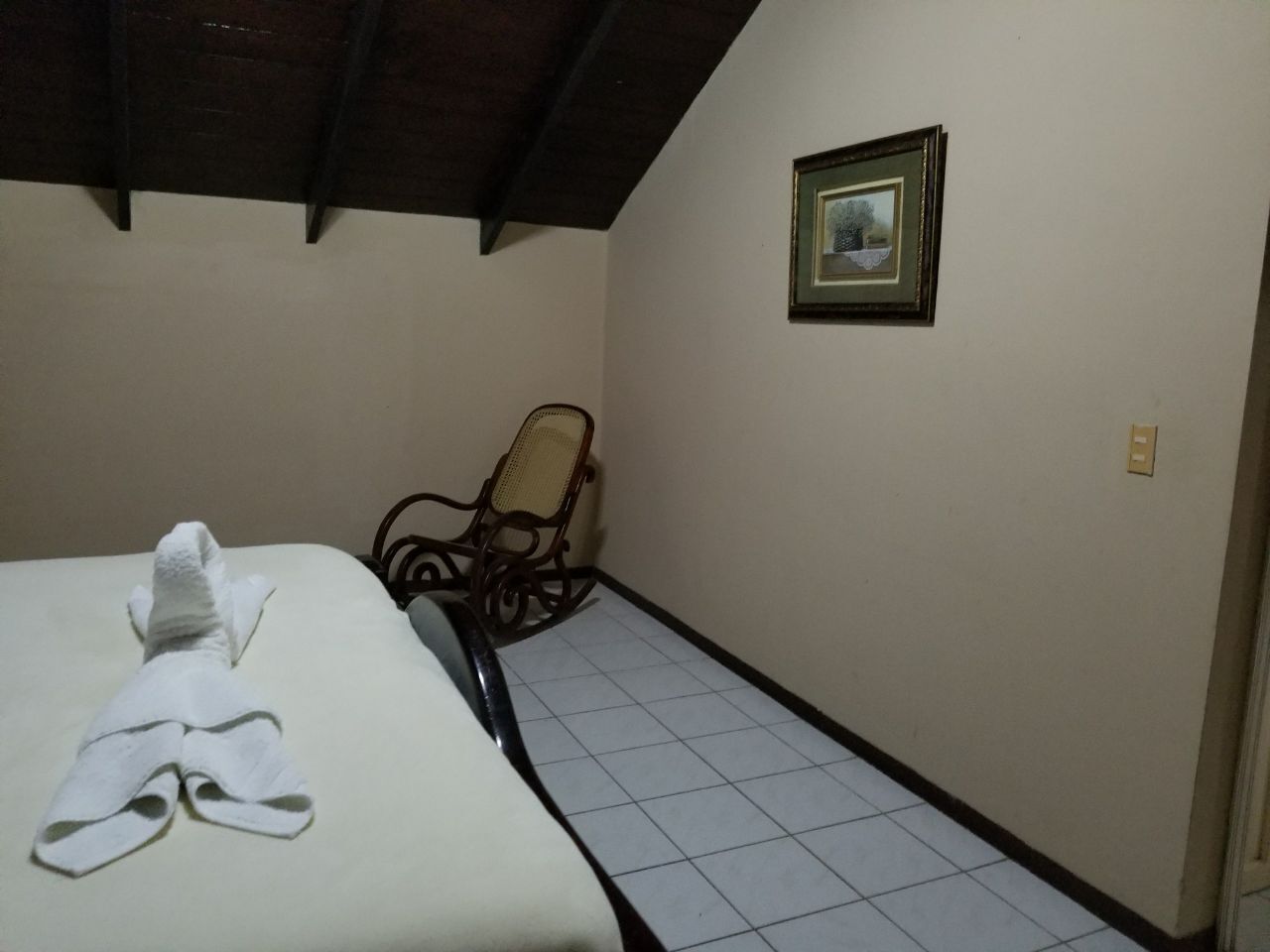 Une chambre d’hôtel avec un lit, une chaise et un tableau encadré au mur.