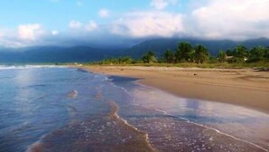 Una playa con cielo despejado, olas y montañas a lo lejos.