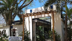 A gated entrance to TAMARINDO BLUE APARTMENTS with a wooden pergola and palm trees. - Only 350 meters from Tamarindo beach and downtown. In quiet and safe area. 
 (Tamarindo)