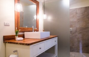 Une salle de bain moderne avec un meuble-lavabo en bois, un lavabo blanc et un grand miroir. Deux lampes suspendues sont fixées au-dessus du miroir, et une serviette est soigneusement pliée sur le meuble-lavabo.