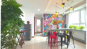 A modern kitchen with a dining area, featuring a colorful floral mural, a potted plant, and a unique light fixture.