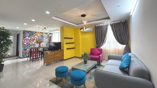 A modern living room with a sofa, ottomans, a TV, and a vibrant floral wall.