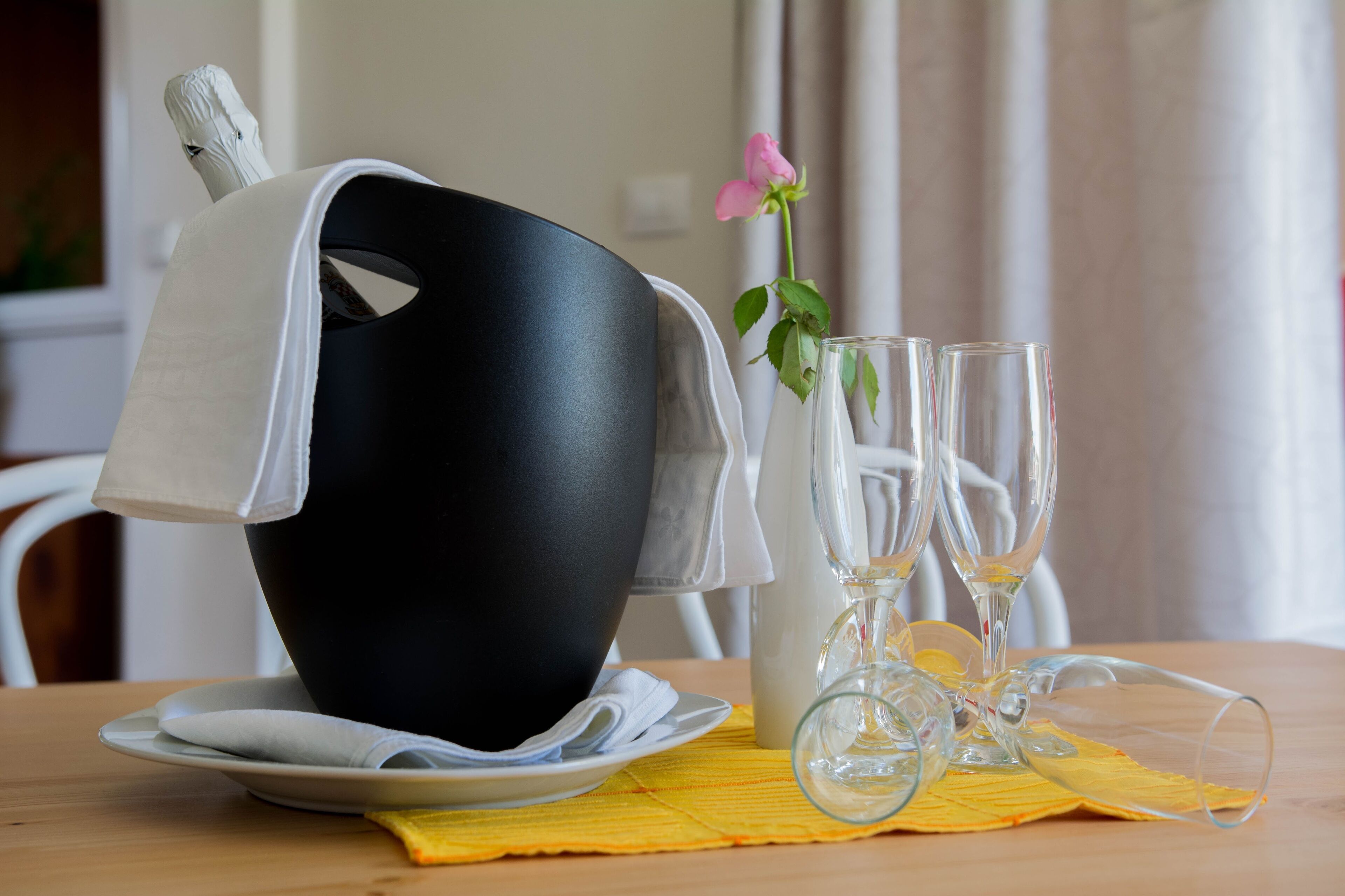 A dining table with a black bowl, two wine glasses, and a pink flower.