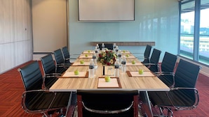 Une salle de conférence avec une longue table, des chaises noires et un écran de projection.