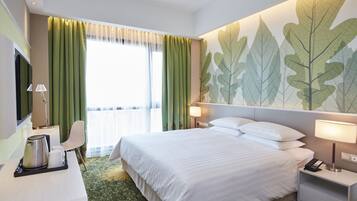 Une chambre d’hôtel avec un grand lit, un bureau avec une lampe, une chaise et un mur orné de motifs végétaux.