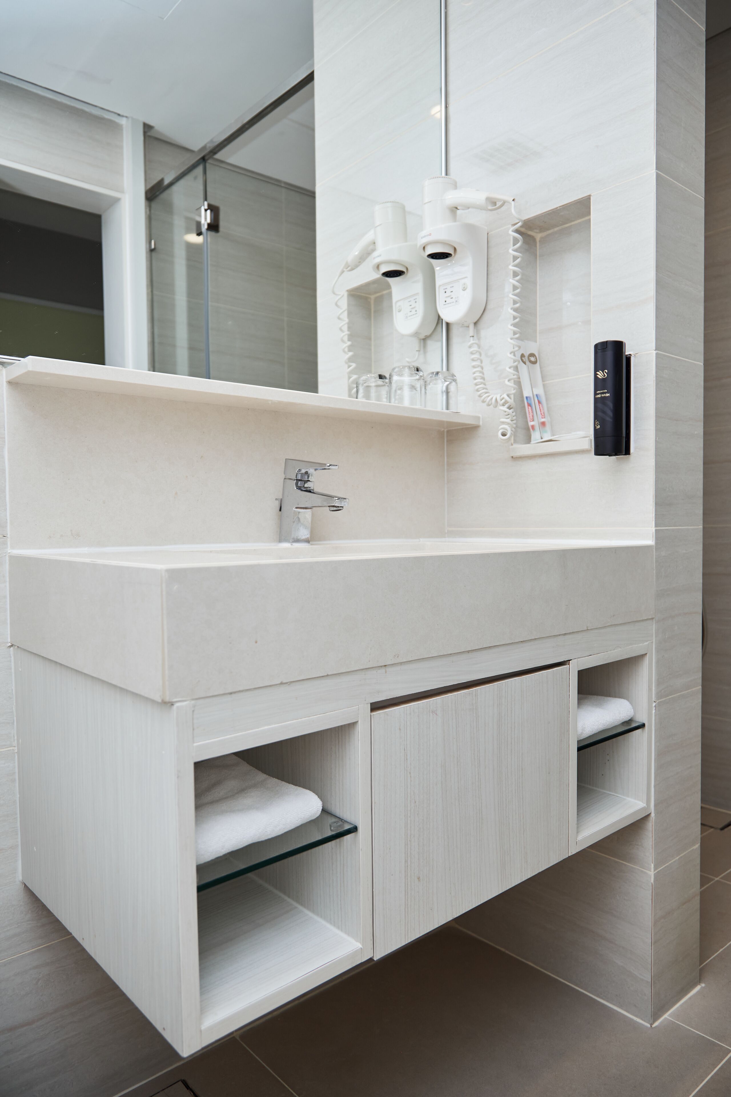 A modern bathroom with a white vanity, a large mirror, and built-in towel racks.