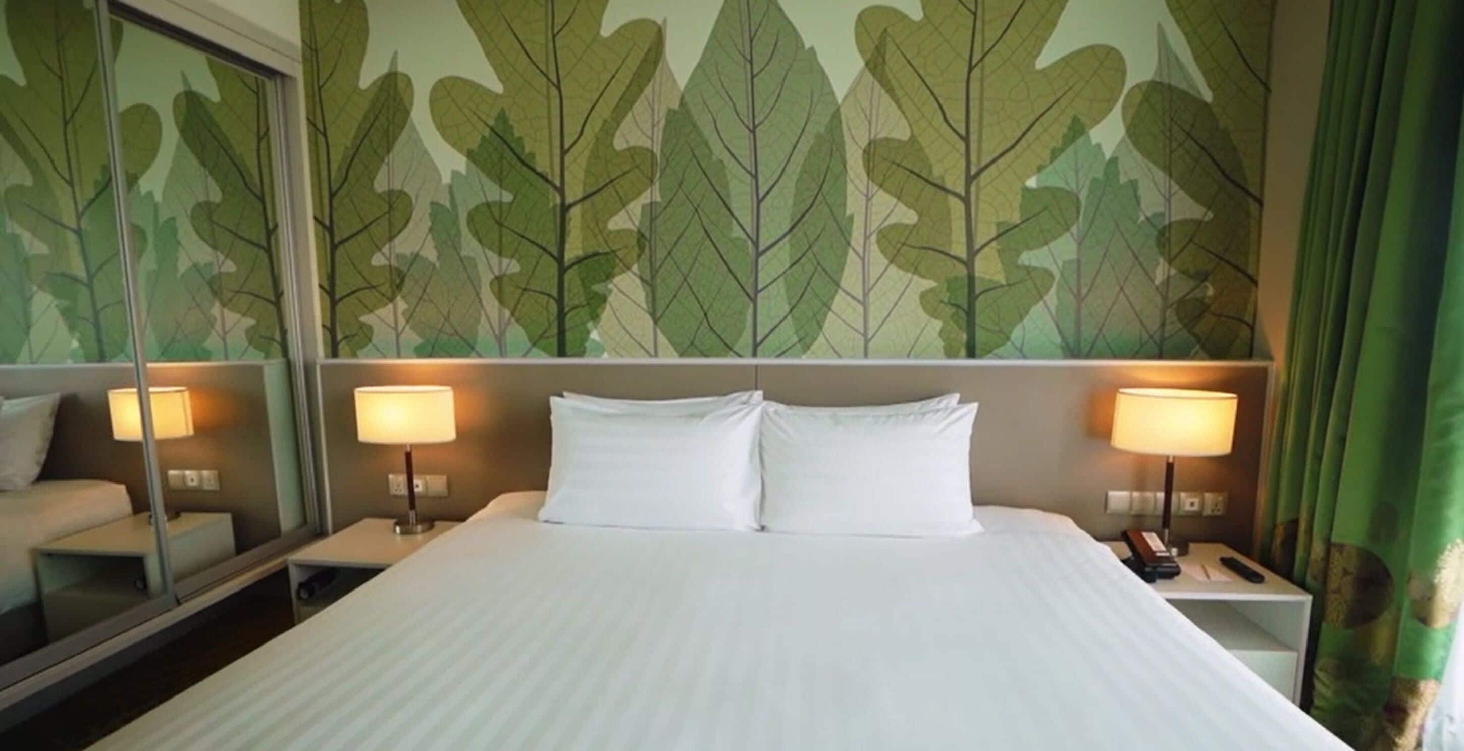 A hotel room with a large bed, two bedside lamps, a nightstand, and a mirror reflecting the room.