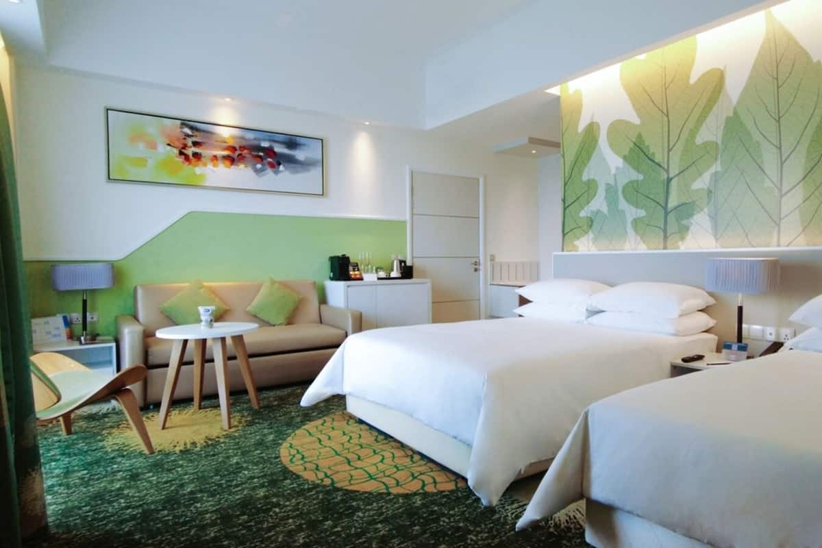 Een hotelkamer met twee bedden, een bank, een kleine tafel en een groen vloerkleed.