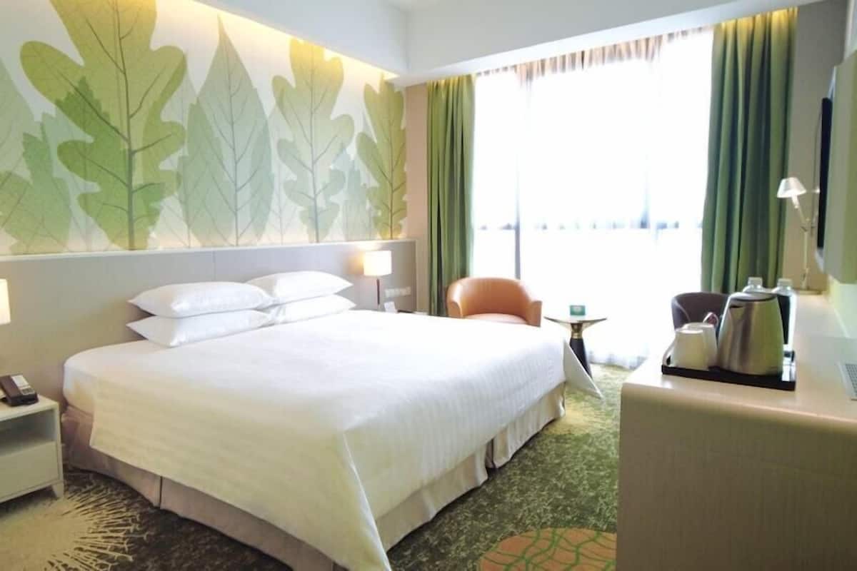 Een hotelkamer met een groot bed, een bureau met lamp, een stoel en een koffiezetapparaat.