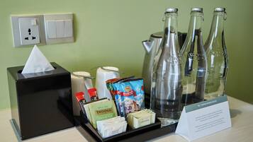 Bandeja com amenidades do quarto de hotel, incluindo caixa de lenços, sachês de chá, leite condensado e água engarrafada.