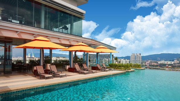 Une piscine à débordement située sur le toit, avec des chaises longues et des parasols, offrant une vue panoramique sur la ville.
