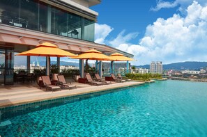 Une piscine à débordement située sur le toit, avec des chaises longues et des parasols, offrant une vue panoramique sur la ville.