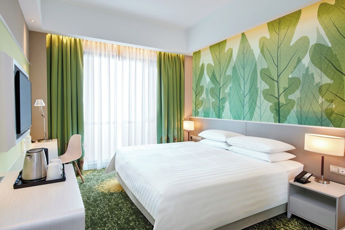 Een hotelkamer met een groot bed, een bureau met koffiezetapparaat, een stoel en een televisie.
