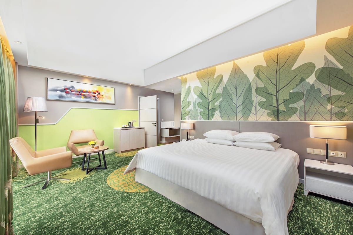 Hotelkamer met een bed, een bureau, een stoel, een lamp en een muur met bladmotief.