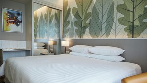 Une chambre d’hôtel avec un grand lit, une table de chevet, une lampe et un mur orné d’un motif de feuilles.