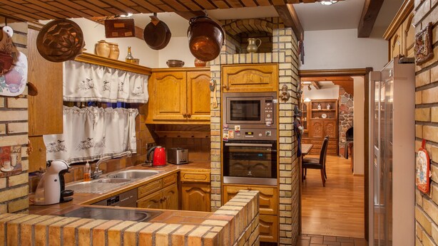 Une cuisine avec des meubles en bois, un îlot central en briques et un mur en pierre.