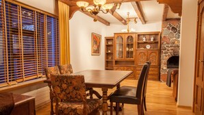 Un coin repas avec une table et des chaises en bois, une cheminée en pierre et une grande fenêtre équipée de stores.