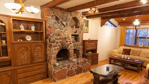 Un salon chaleureux avec une cheminée en pierre, des meubles en bois et une grande fenêtre agrémentée de rideaux.