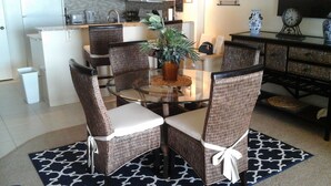 A dining area with a round glass table surrounded by wicker chairs with white cushions. - Beautiful Beachfront Getaway retreat for couples, Private Balcony & Sunsets #202 (Indian Shores)