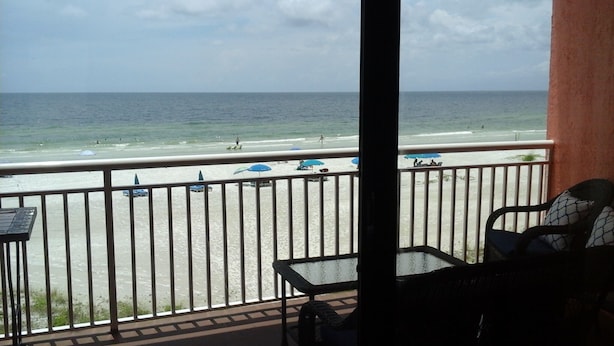 A balcony with a view of the beach, featuring a railing, a table, and a chair. - Beautiful Beachfront Getaway retreat for couples, Private Balcony & Sunsets #202 (Indian Shores)