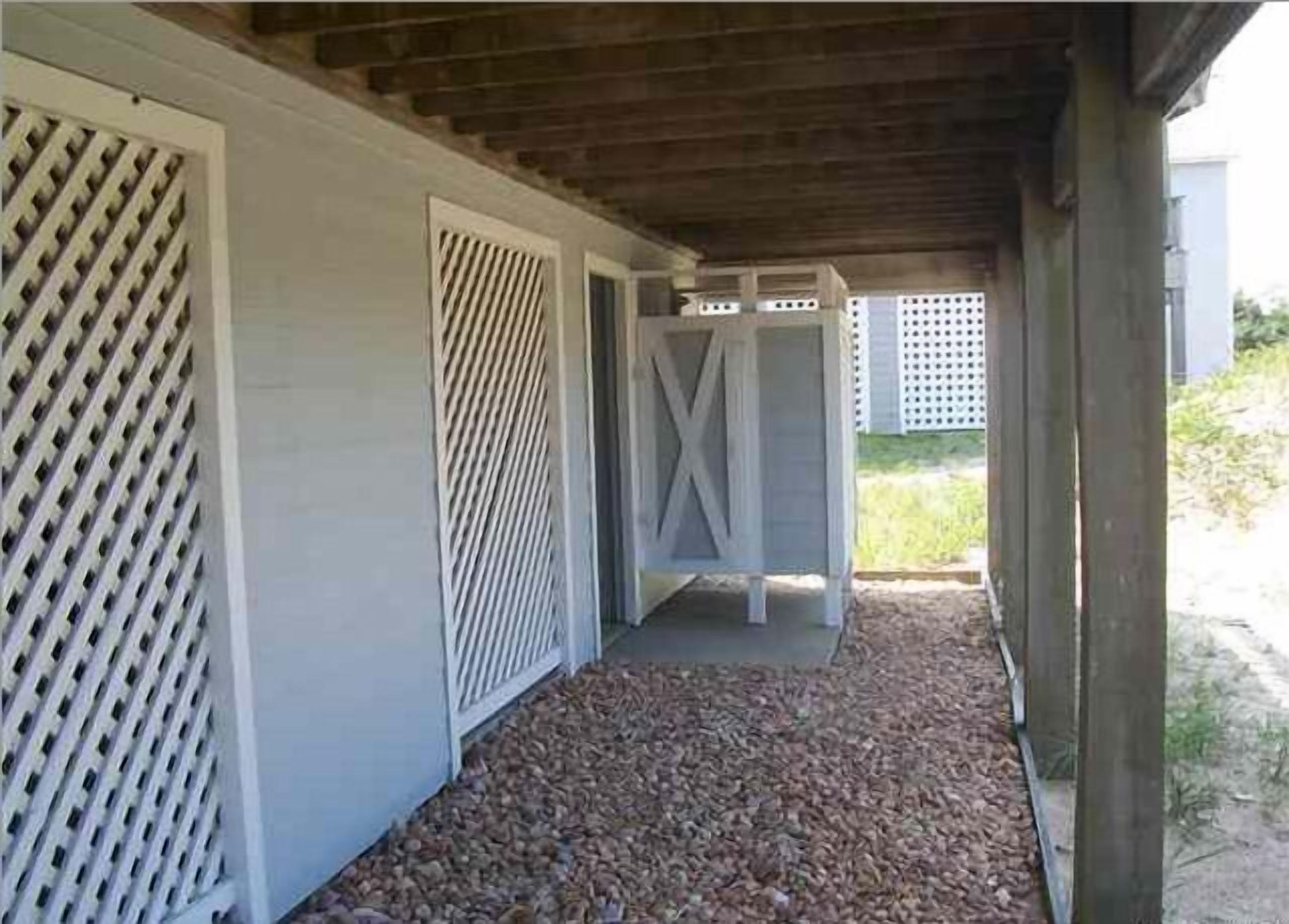 A covered outdoor area with a gravel path, white lattice panels, and a wooden structure.