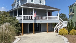 A two-story house with a porch, an American flag, and a staircase leading to the second floor. - Beautiful OBX house on golf course with sunset views and Beach Club access (Nags Head)