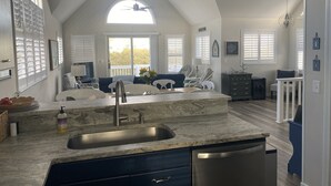 A kitchen with a marble countertop, stainless steel sink, and a dishwasher. There is a ceiling fan and a window with blinds. - Beautiful OBX house on golf course with sunset views and Beach Club access (Nags Head)