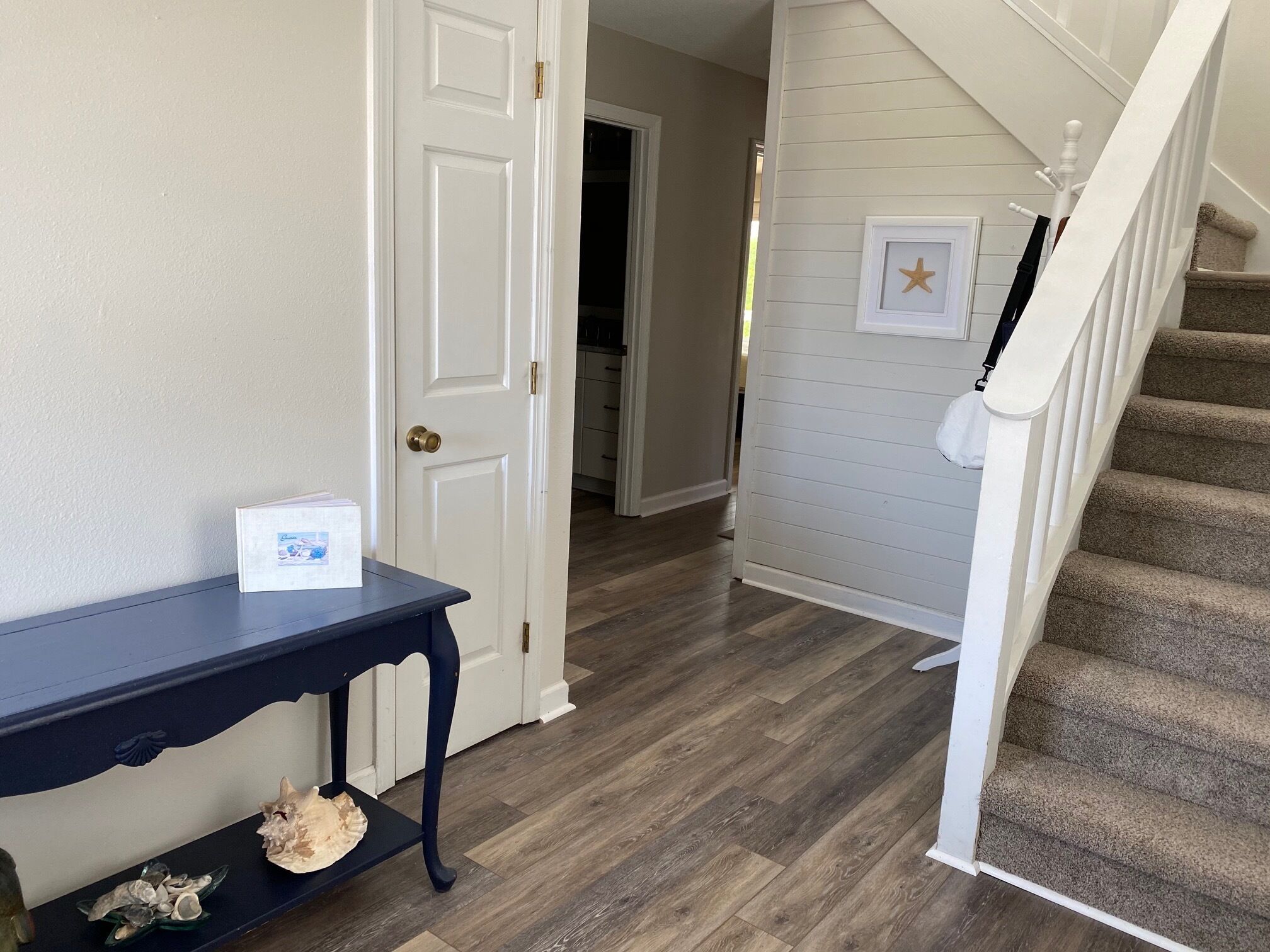 A hallway with a dark blue console table, a white door, and a staircase with a beige carpet.