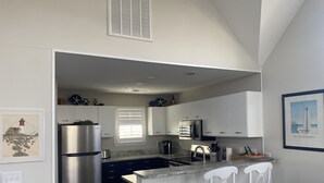 A modern kitchen with stainless steel appliances, white cabinetry, and a bar area with white chairs. - Beautiful OBX house on golf course with sunset views and Beach Club access (Nags Head)