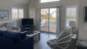 A spacious living room with a television, a sofa, and two wicker chairs. - Beautiful OBX house on golf course with sunset views and Beach Club access (Nags Head)