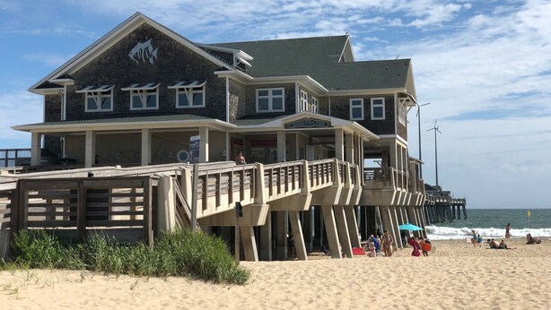 A beachfront pier with a restaurant named "Jennette's Pier" featuring a stone facade and multiple decks. - Beautiful OBX house on golf course with sunset views and Beach Club access (Nags Head)