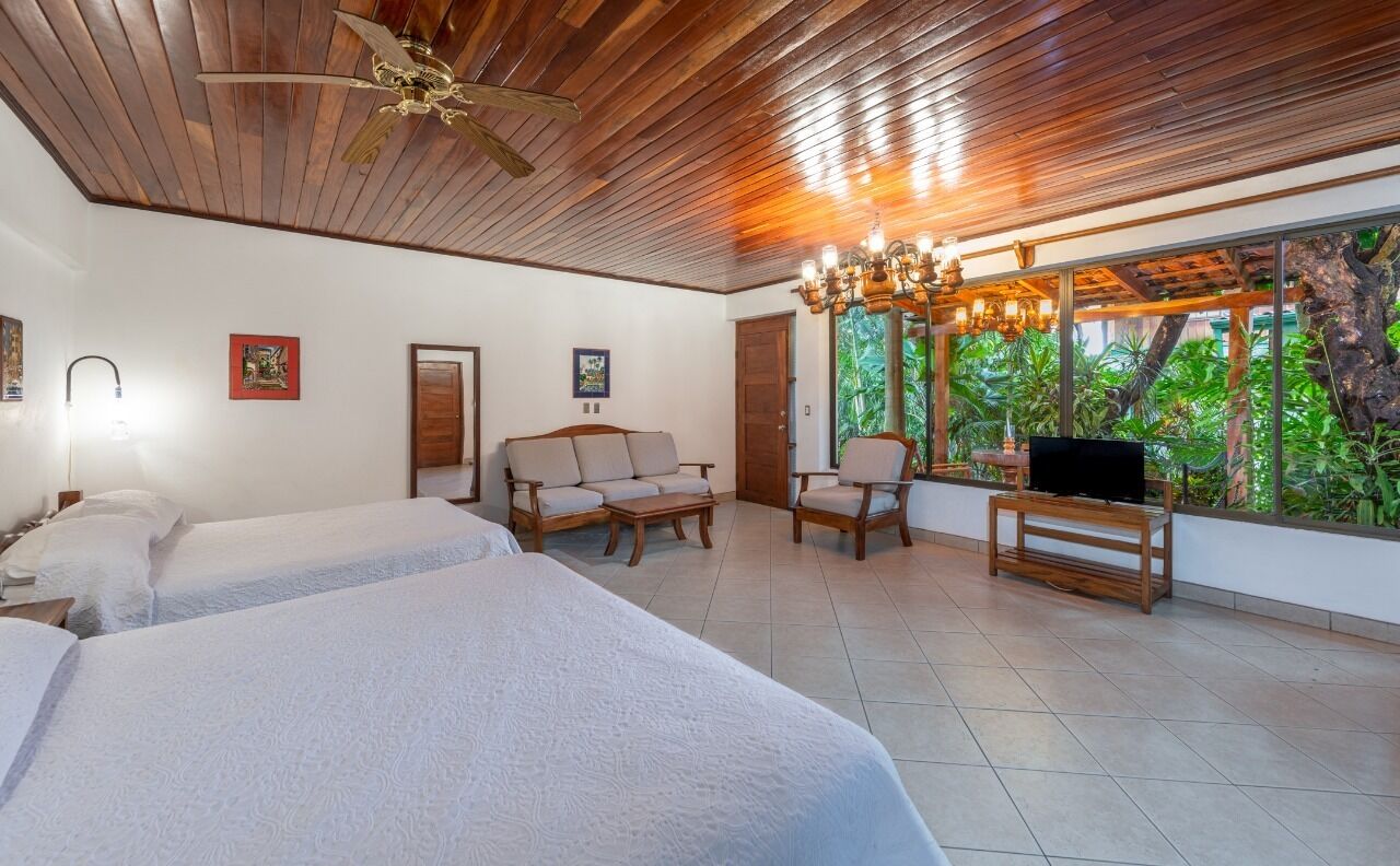 Camera d'albergo con due letti, soffitto in legno, un lampadario, televisione e vista sul verde.