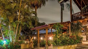 A covered outdoor area with a wooden pergola, surrounded by lush tropical plants and palm trees. - Escazu Vacation  Rentals, Studio Apartments and standard rooms (San Jose)
