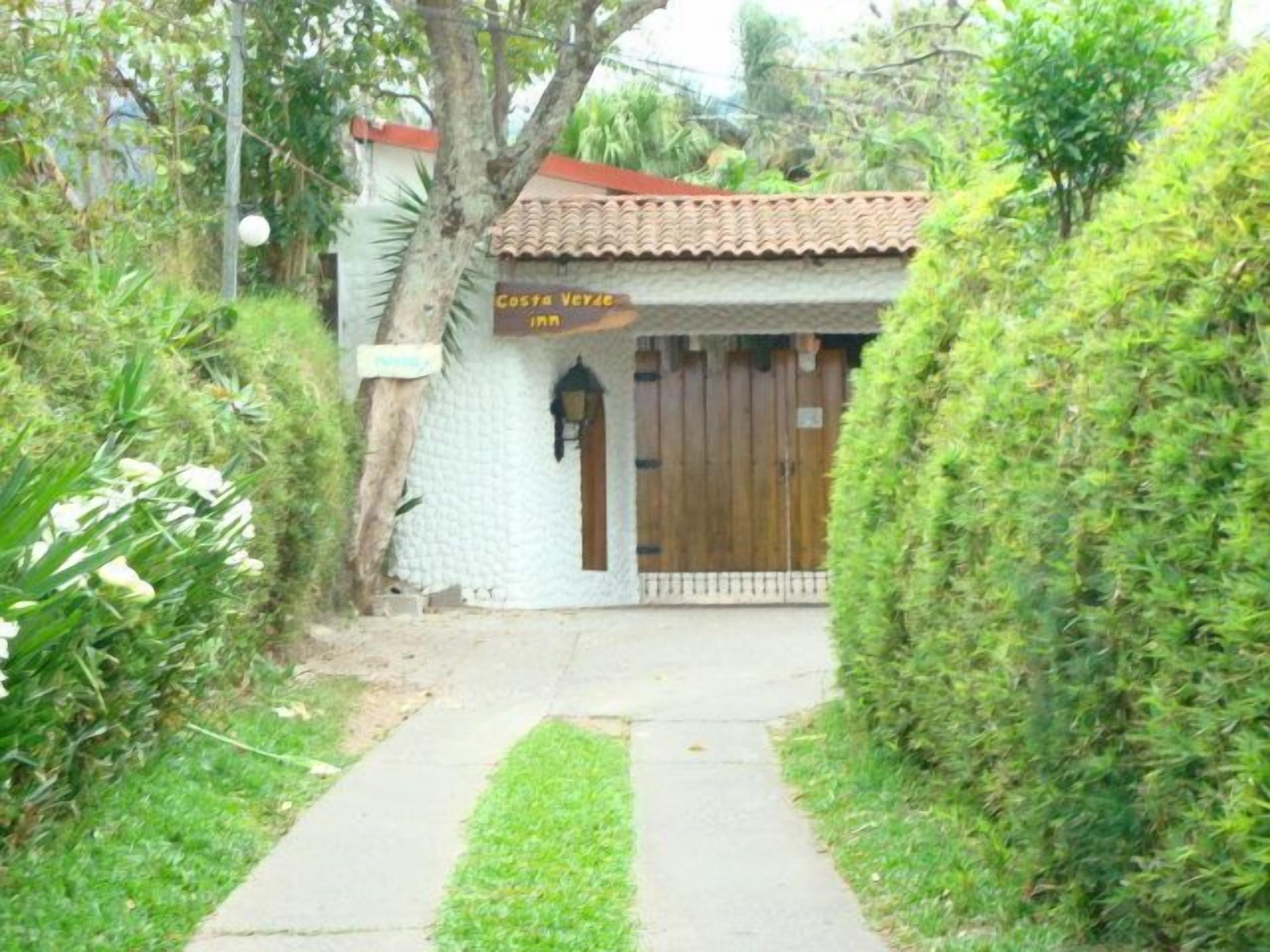 Un chemin menant à un bâtiment doté d’un toit en tuiles et d’une enseigne sur laquelle on peut lire « Costa Verde ».