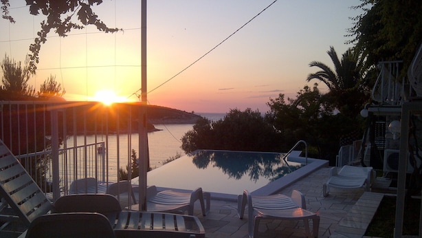 Un espace aménagé au bord de la piscine, avec des chaises longues et une vue sur le coucher de soleil sur l’eau.