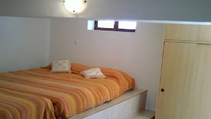 Une chambre à coucher avec un lit, deux oreillers, une armoire en bois et une petite fenêtre.