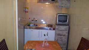 Une petite cuisine équipée d’un évier, d’une cuisinière et d’un petit réfrigérateur. On y trouve une table sur laquelle sont posés une télécommande et un verre.