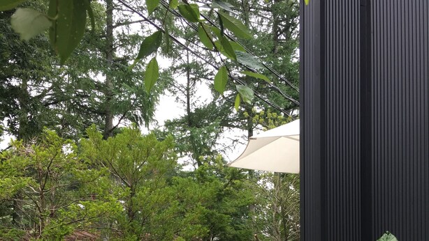 A wooden deck with a table and chairs, surrounded by greenery and a black wall. - Wistaria Karuizawa (Karuizawa)