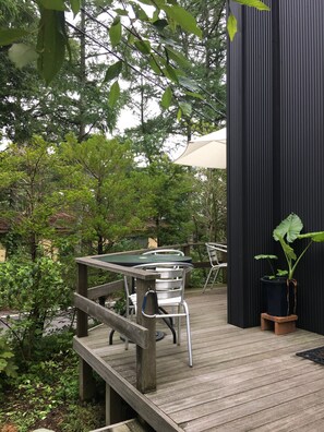 A wooden deck with a table and chairs, surrounded by greenery and a black wall. - Wistaria Karuizawa (Karuizawa)