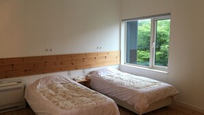 A bedroom with two single beds, a wooden headboard, a small bedside table, and a window with a view of greenery. - Wistaria Karuizawa (Karuizawa)